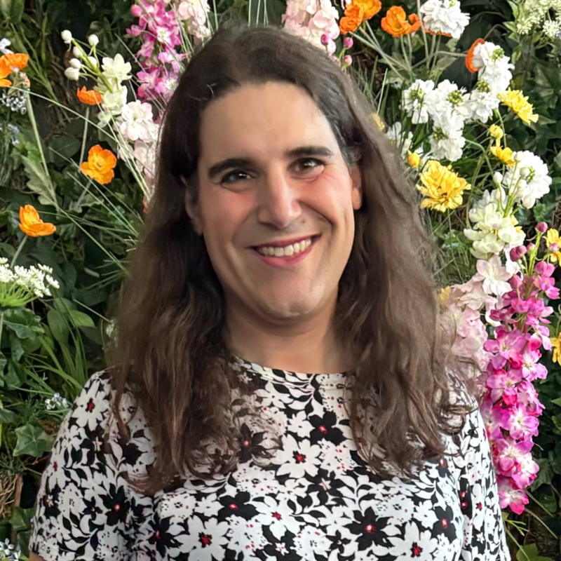An image of me, Paulina Duarte, wearing a white and black floral dress in front of a wall of flowers.